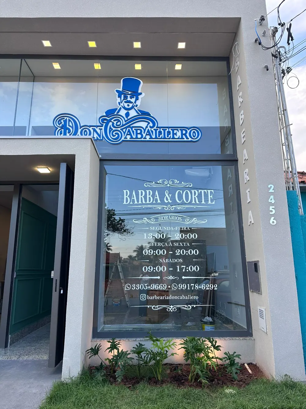 Entrada da barbearia com o logotipo do cavalheiro de cartola e a vitrine Barba e Corte