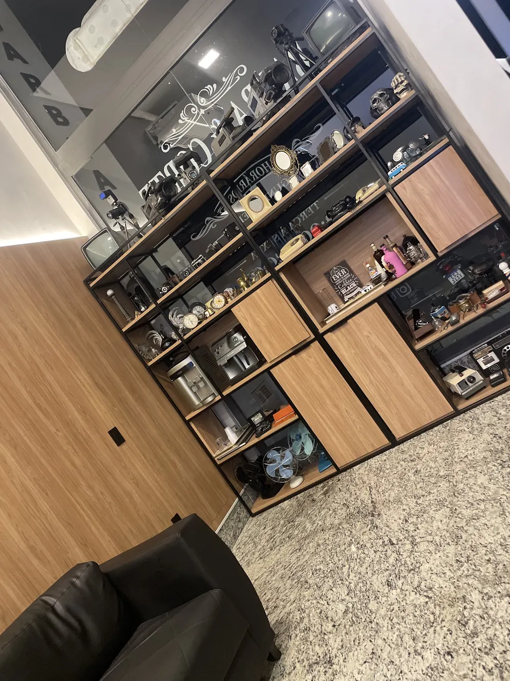 Estante de madeira com nichos e produtos ao lado de uma poltrona preta